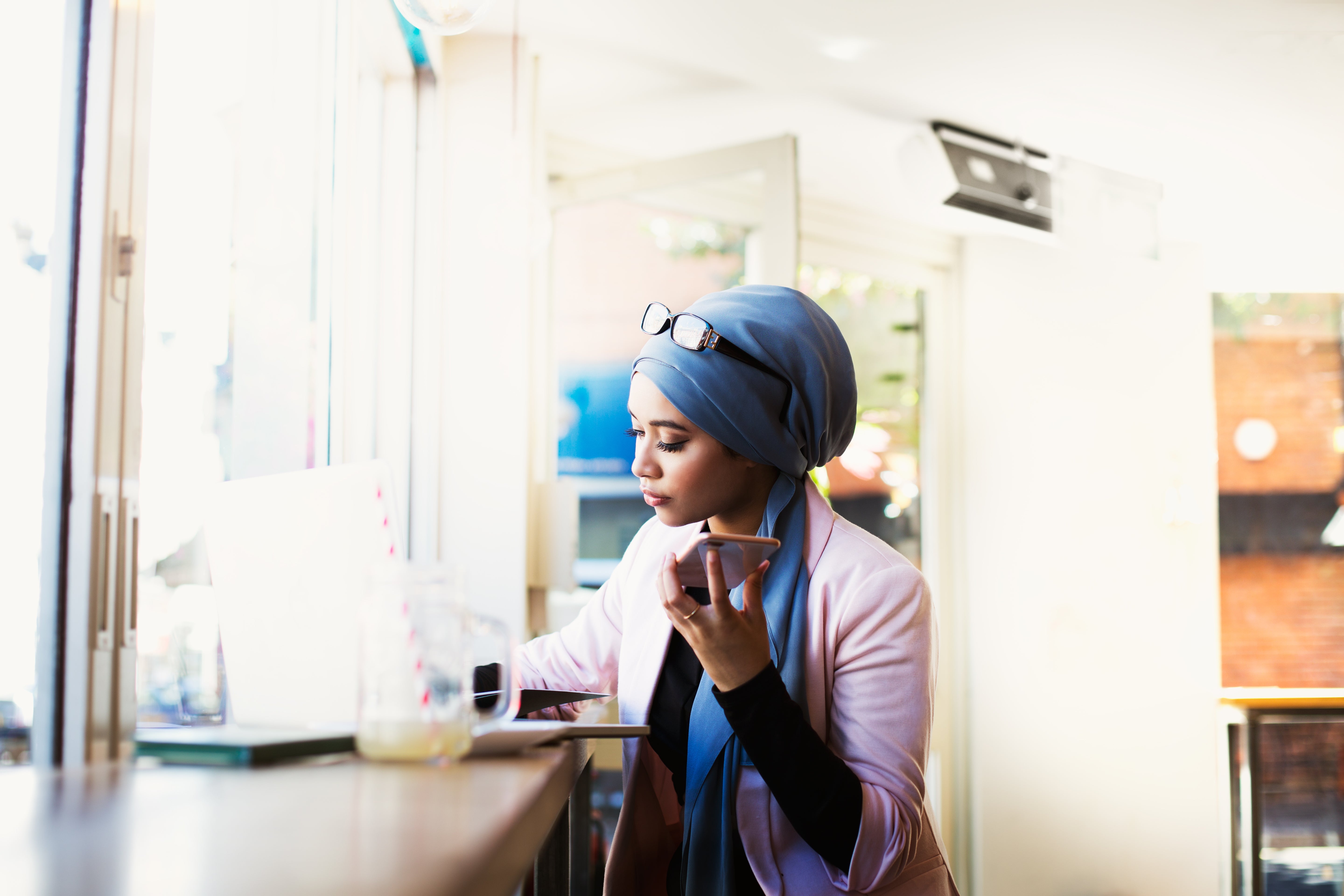 Person i et stilig antrekk jobber på en bærbar datamaskin på en kafé, og holder en kaffekopp, med briller på hodet