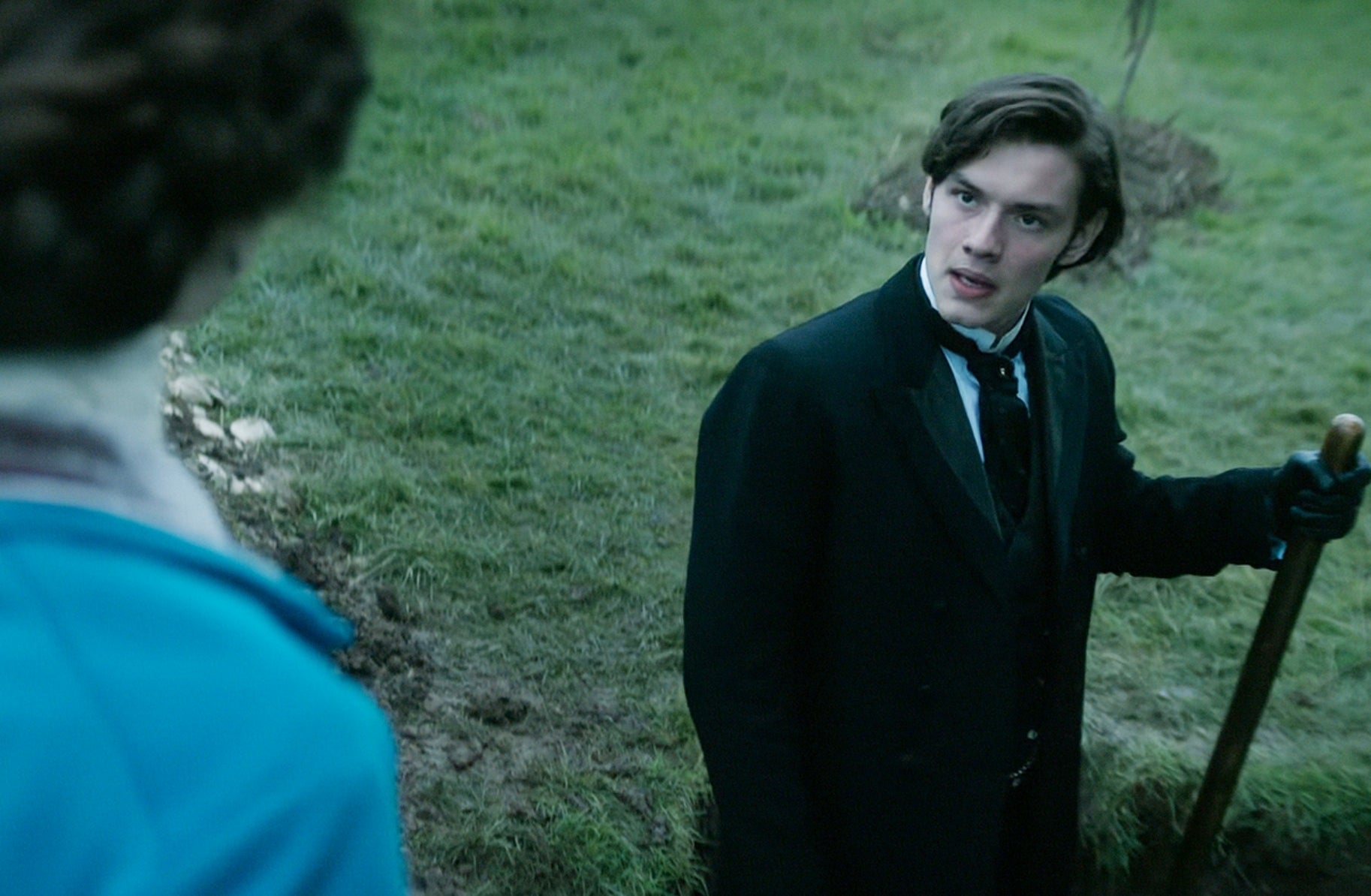 Period drama scene showing a man in a 19th-century suit holding a shovel, speaking to a woman in frame