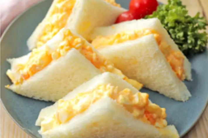 お皿に盛られた卵サンドイッチと付け合せのプチトマト、葉物野菜。
