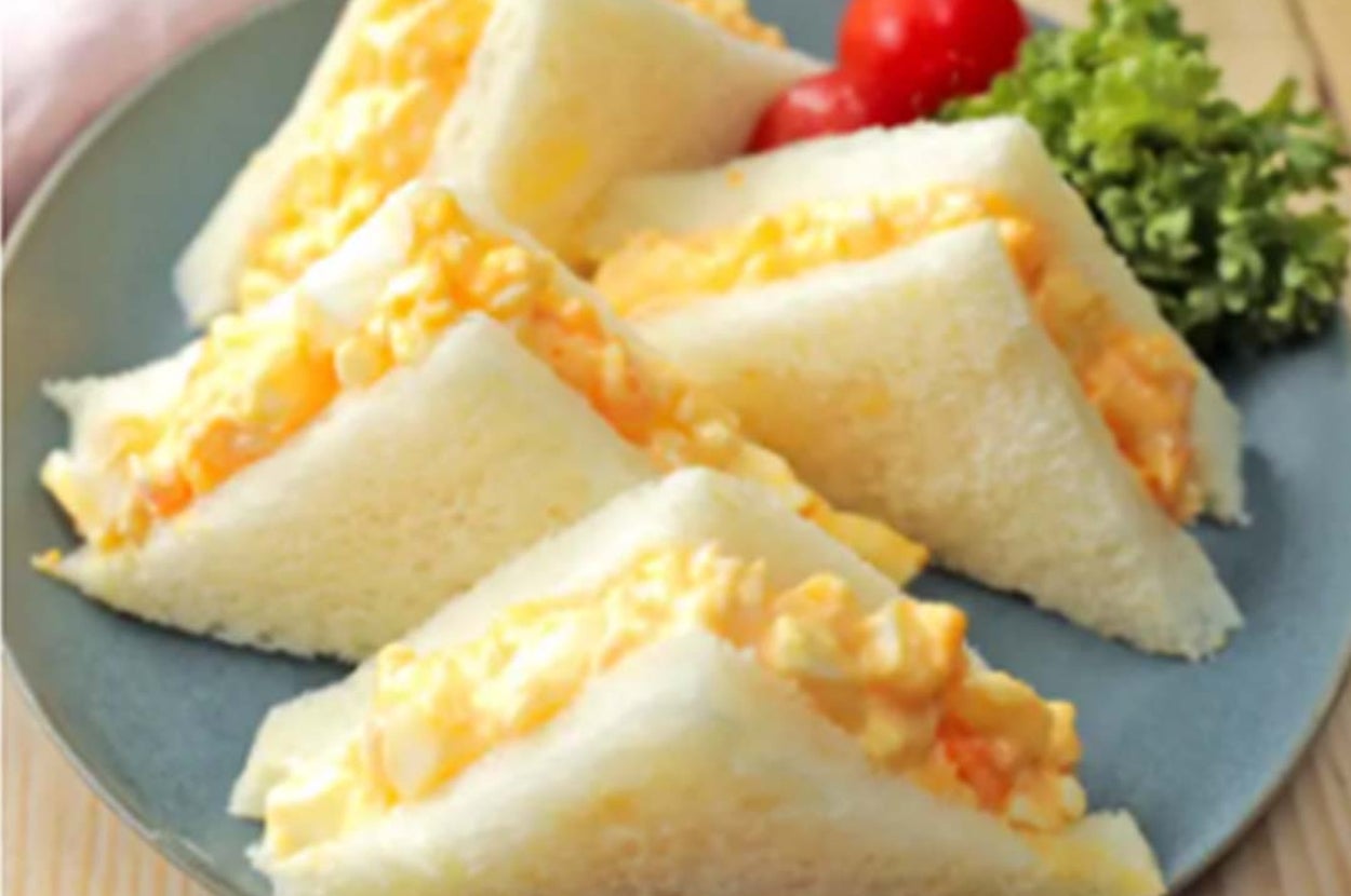 お皿に盛られた卵サンドイッチと付け合せのプチトマト、葉物野菜。