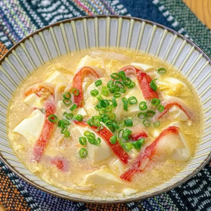 豆腐とカニカマのスープが器に盛られている。刻みネギがトッピングされている。