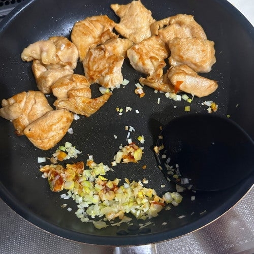 鶏肉と刻んだ玉ねぎ、ニンニクがフライパンで調理されている様子。調理中の家庭料理の一場面。