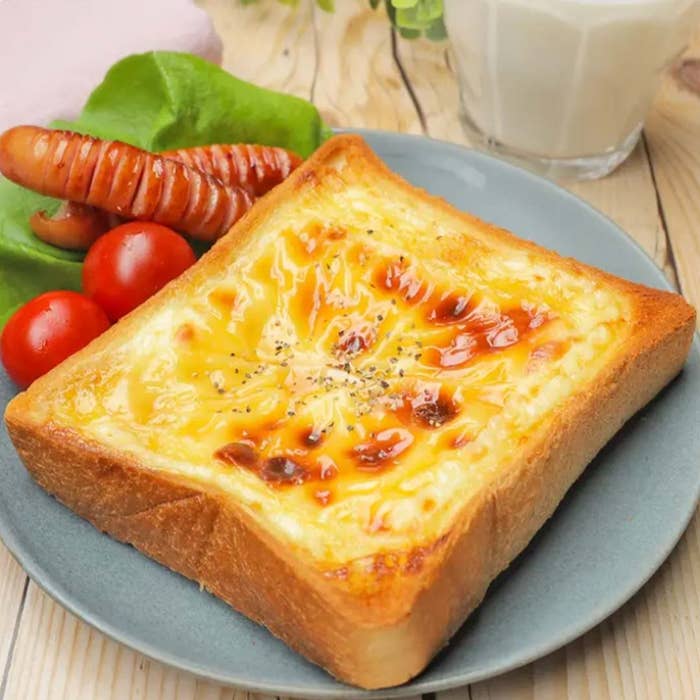 トーストにチーズが溶けており、ウインナーとプチトマトが添えられた食事プレート。背景にグラス入りの飲み物。