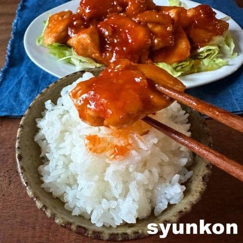料理の写真。チキンの甘辛ソース炒めが皿に盛られ、白ご飯に載せられようとしている。