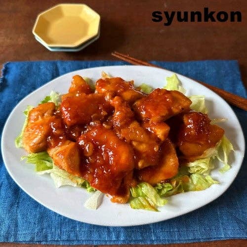 テーブルに青いランチョンマットと皿。レタスの上にソースがかかった鶏肉料理があり、縁に小皿と箸が置かれている。