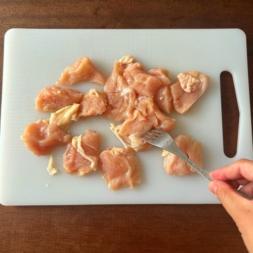 まな板の上にカットされた鶏肉とそれをフォークで刺している手の写真。