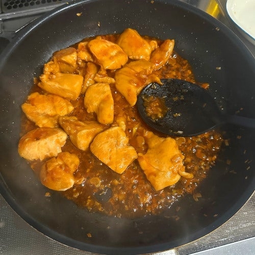 フライパンで料理されている鶏肉の炒め物。ソースが全体に絡まっている。