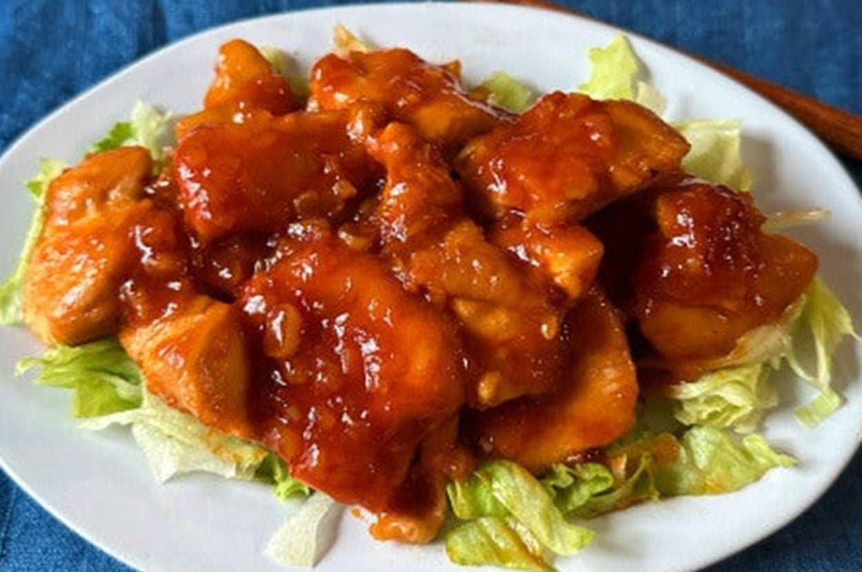 皿に盛られた甘辛ソースのチキンがレタスの上に乗っている。食卓に箸が添えられている。