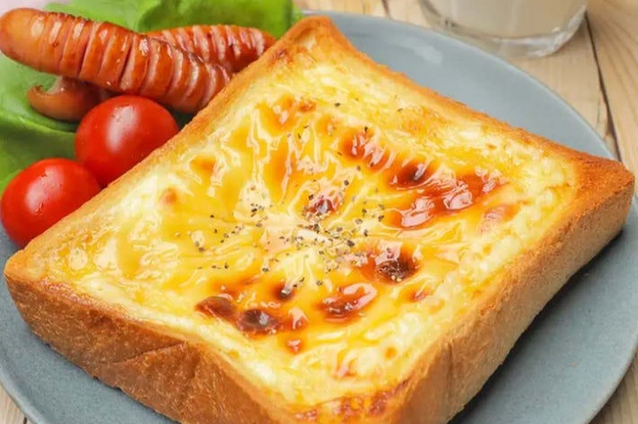 トーストに溶けたチーズ、スライスソーセージ、レタス、トマトが添えられた朝食プレート。後ろにグラスミルク。