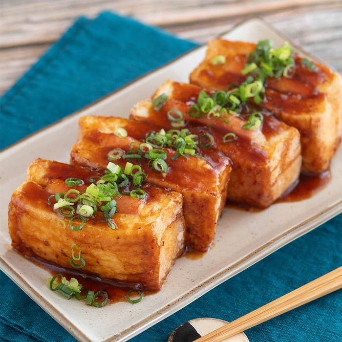 皿に盛られた揚げ豆腐の上にネギとソースがかけられている。食卓に箸が添えられている。