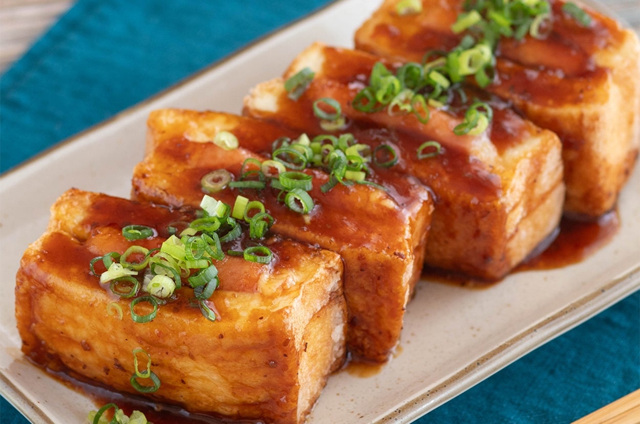 揚げ出し豆腐に甘辛いタレと刻みネギがのった料理が皿に盛られている。添えられた箸。