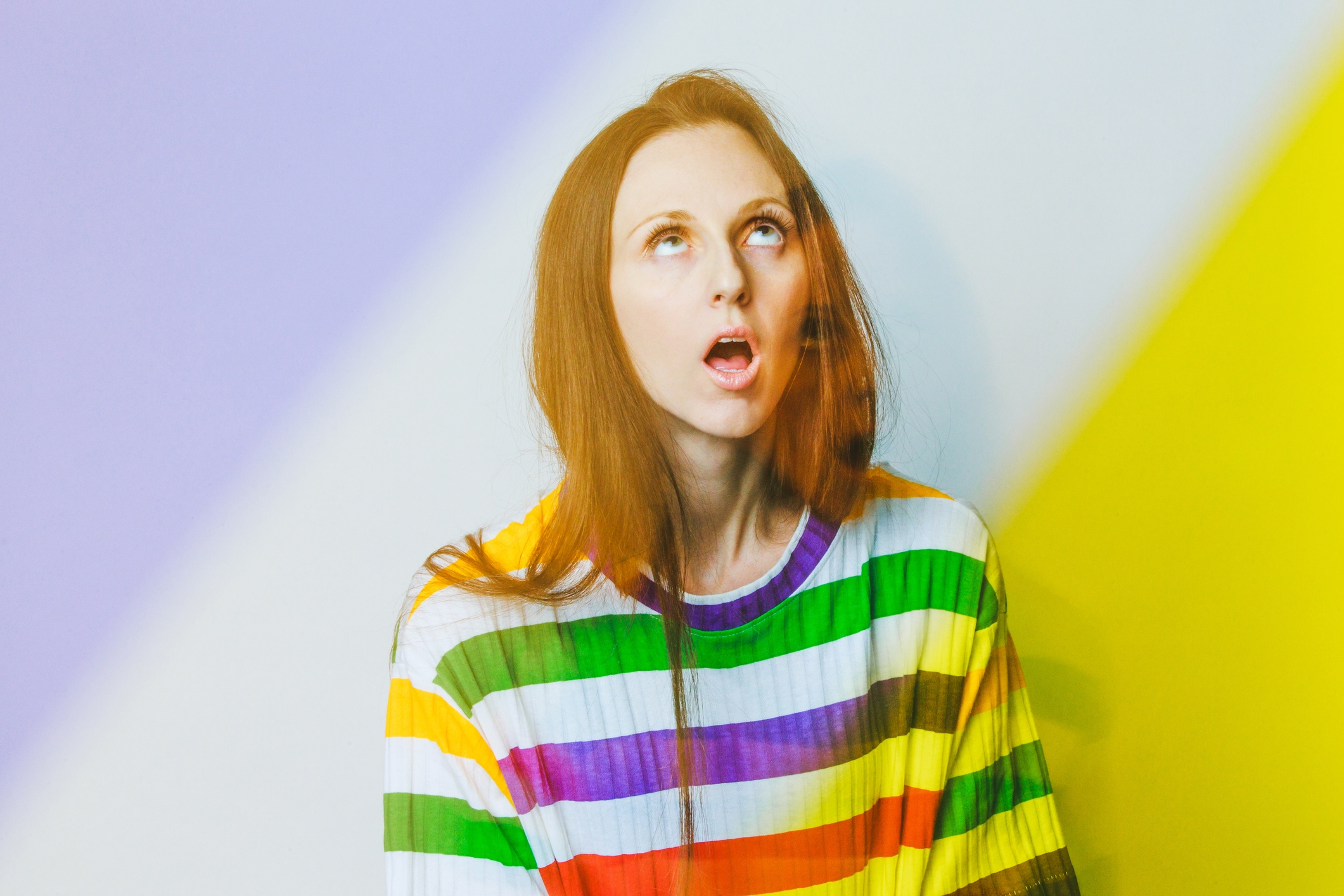 Personen ser opp med en åpen munn, iført en skjorte med dristige horisontale striper. Diagonale lysstriper legger ut bildet