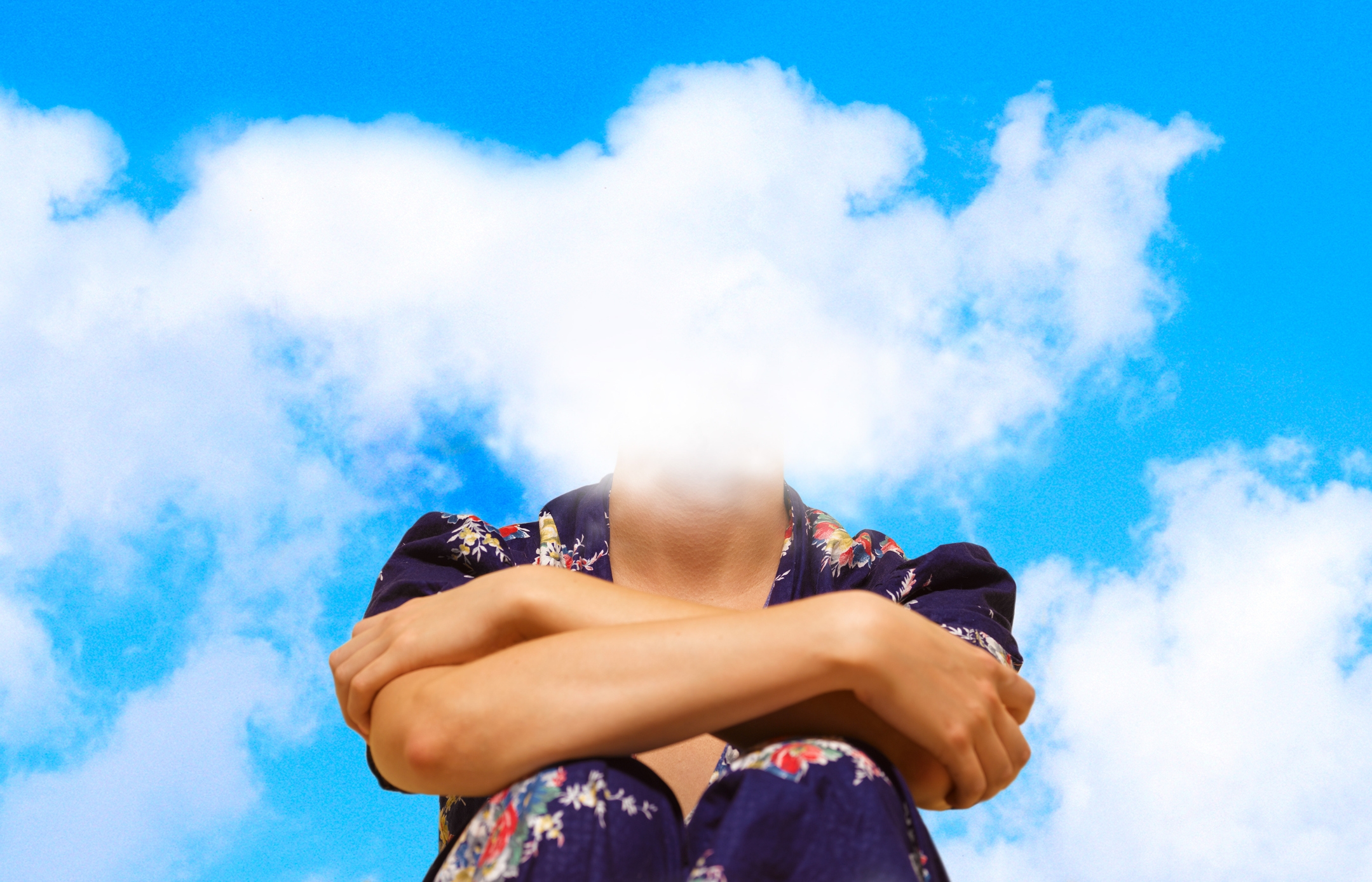Person som sitter med armene krysset, hodet erstattet av skyer, iført en blomstermønstret topp mot en overskyet himmel