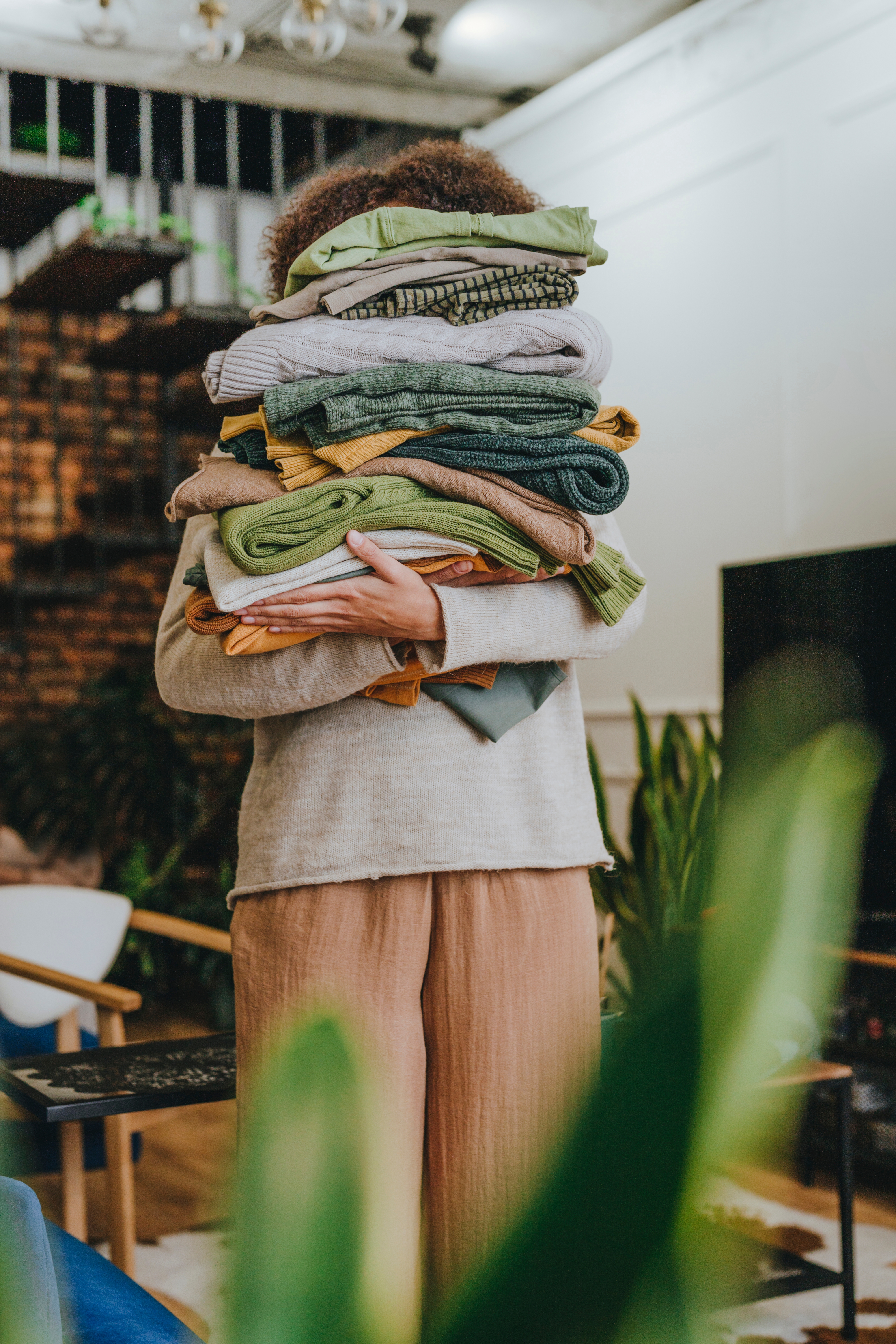 Person som bærer en stor haug med brettet vaskeri, delvis dekker ansiktet, i en koselig stue -omgivelser
