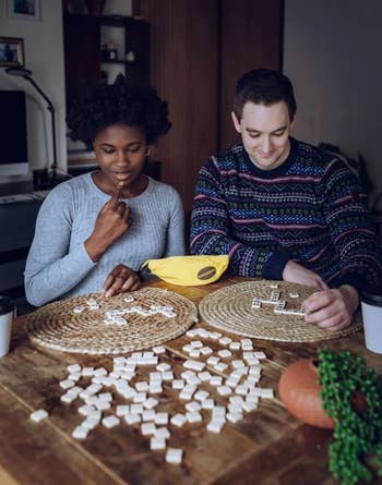 Two radical beryllium astatine a array playing a connection tile game. One has a festive sweater, and the array has a plant