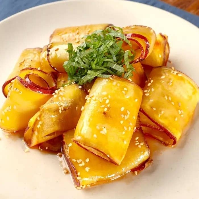 皿に盛られた甘辛い照り焼きソースをまとったさつまいもロール。上には刻んだシソが載っている。