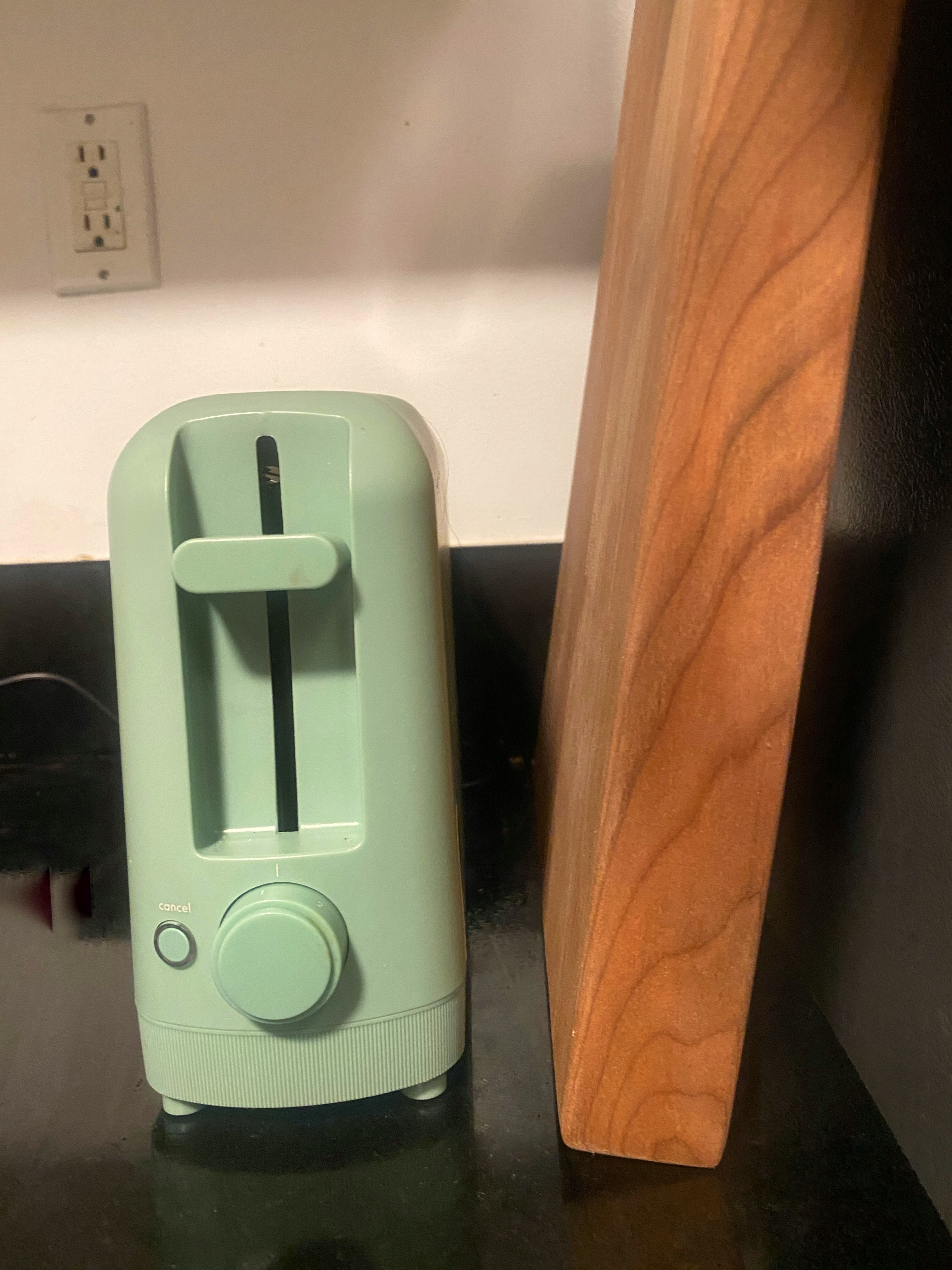 A toaster with a rounded design and a large dial next to a wooden cutting board on a kitchen counter