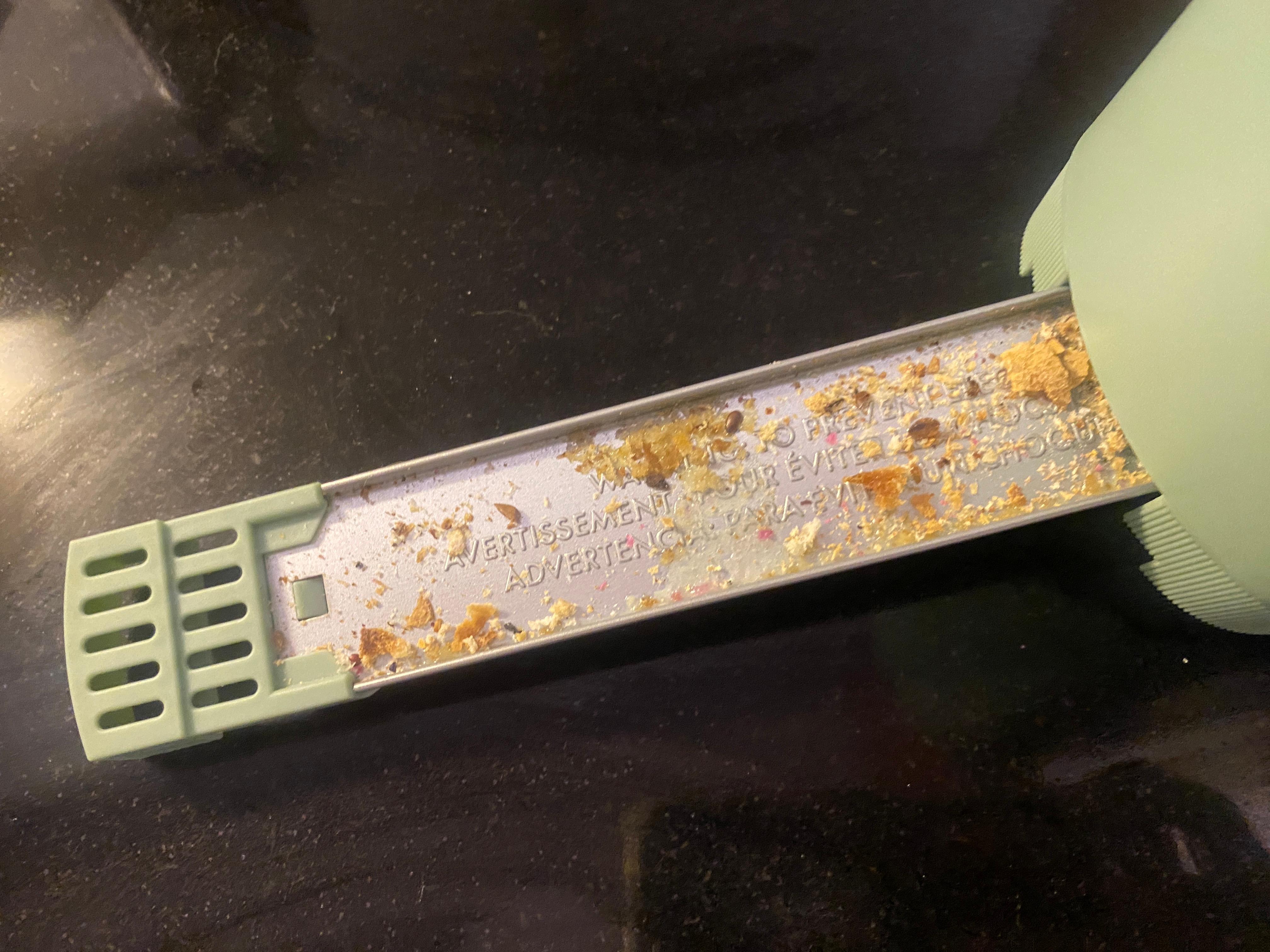 Close-up of a crumb-filled, removable metal tray from an appliance, placed on a dark surface