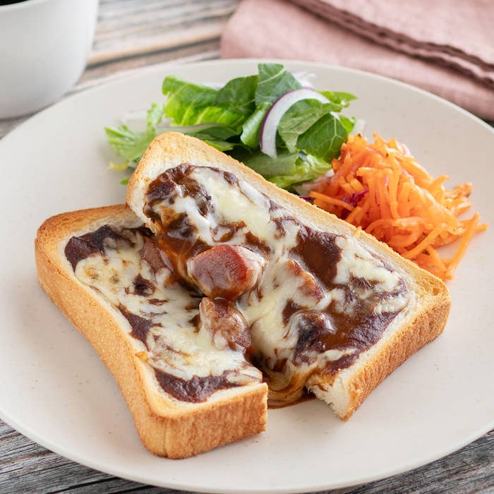 トーストに溶けたチーズとカレー、取り分けられた一切れ。サラダとすりおろしたニンジンが添えられた食事プレート。