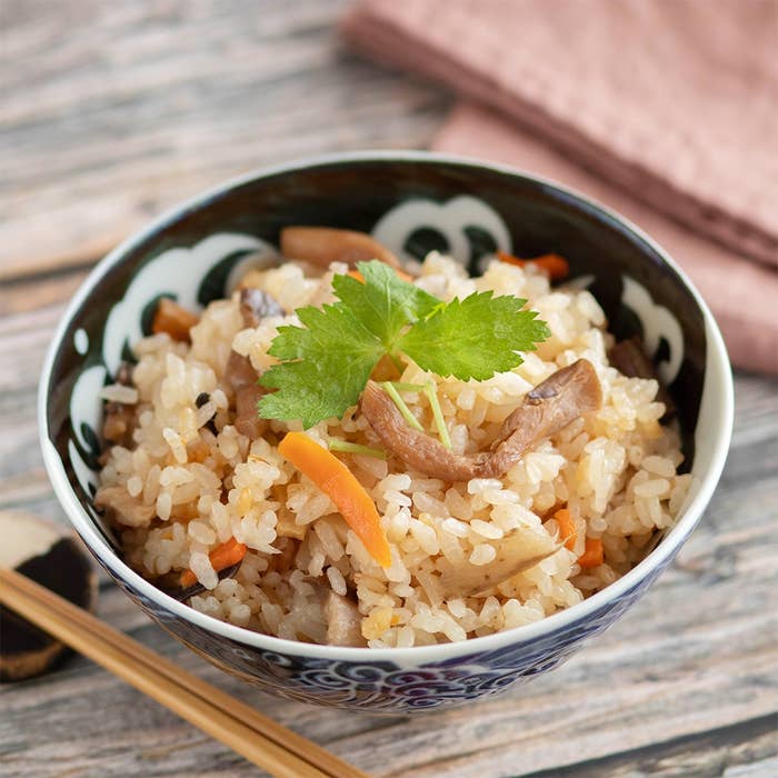 器に盛られた炊き込みご飯がテーブルに置かれている。刻んだ野菜と肉が含まれている。
