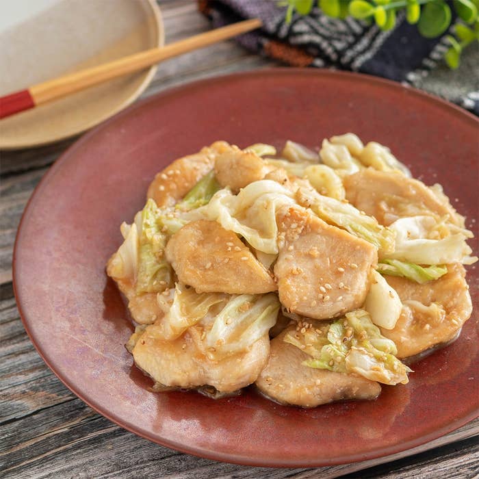 キャベツと鶏肉の炒め物が茶色い皿に盛られている。食卓に箸と小鉢も添えられている。