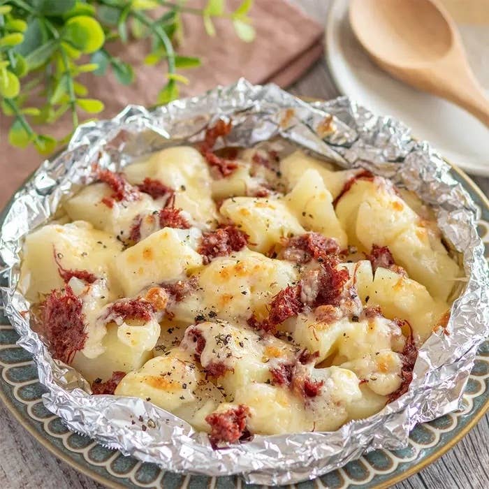 ホイルに包まれたポテトとチーズ、細かい肉のトッピングがオーブンで焼かれている料理。
