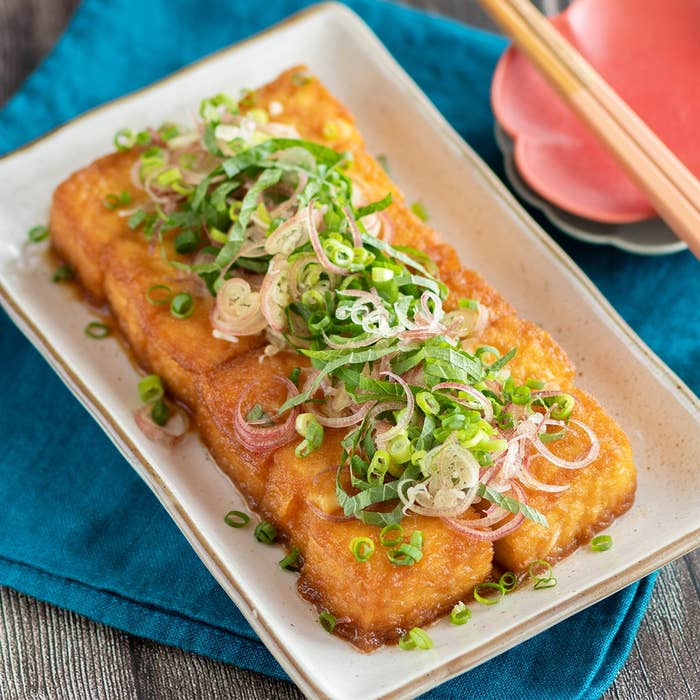 揚げ出し豆腐の上に刻んだネギとショウガがトッピングされた料理が皿に盛られている。