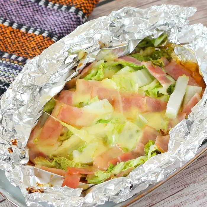 ホイルに包まれたキャベツとハムの上に溶けたチーズが乗った料理。シンプルで美味しそうな家庭料理。