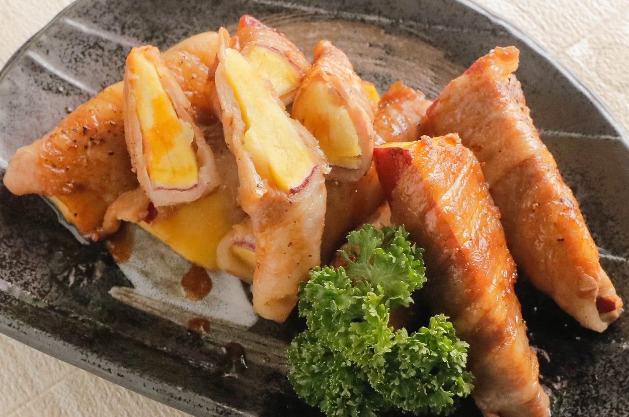 皿に盛られた焼きリンゴとベーコンの巻き物。パセリが添えられている。