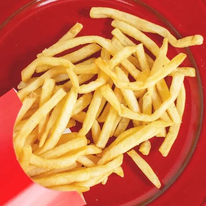 赤い皿に載ったフライドポテトが紙の容器からこぼれています。