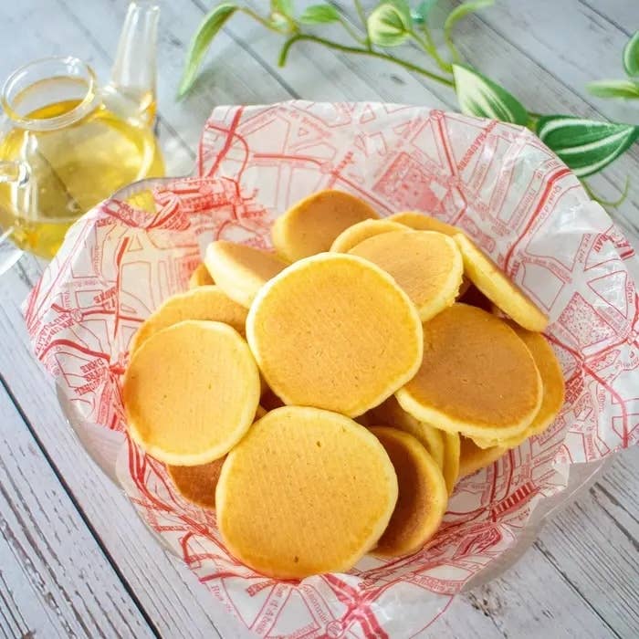 バスケットに盛られた小さなパンケーキとガラス製のオイルポット。背景に植物が見える。