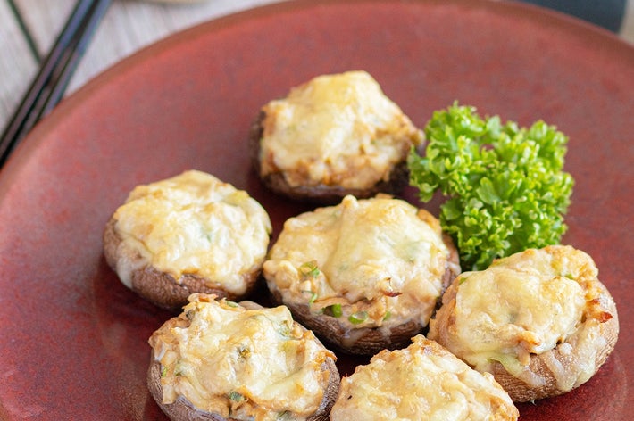 皿に載ったチーズと野菜でトッピングされた焼きマッシュルーム。付け合せにパセリ。