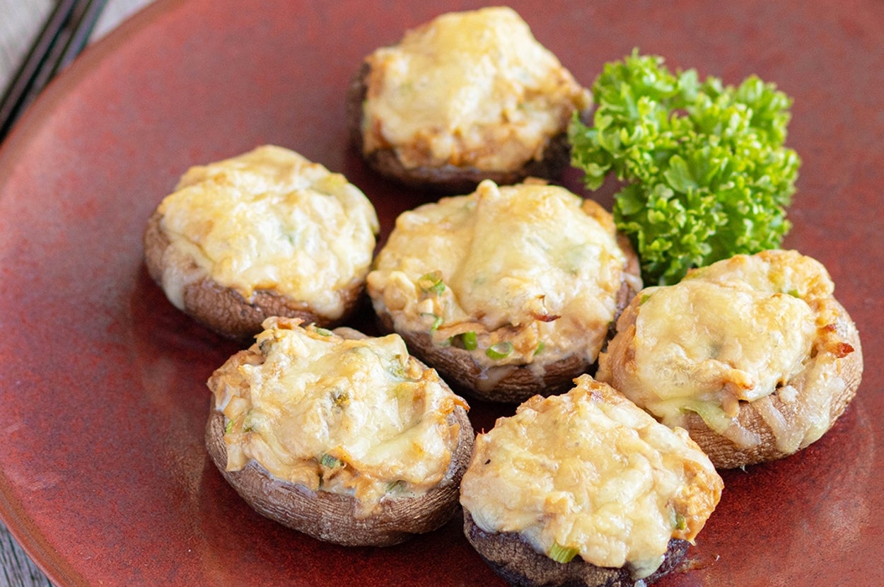 皿に載ったチーズと野菜でトッピングされた焼きマッシュルーム。付け合せにパセリ。