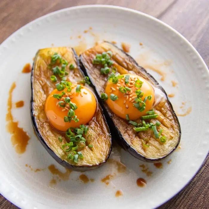 なすの卵黄のせ照り焼き。皿に盛られたなすの半分に卵黄とネギがのっている料理。ソースがかかっている。