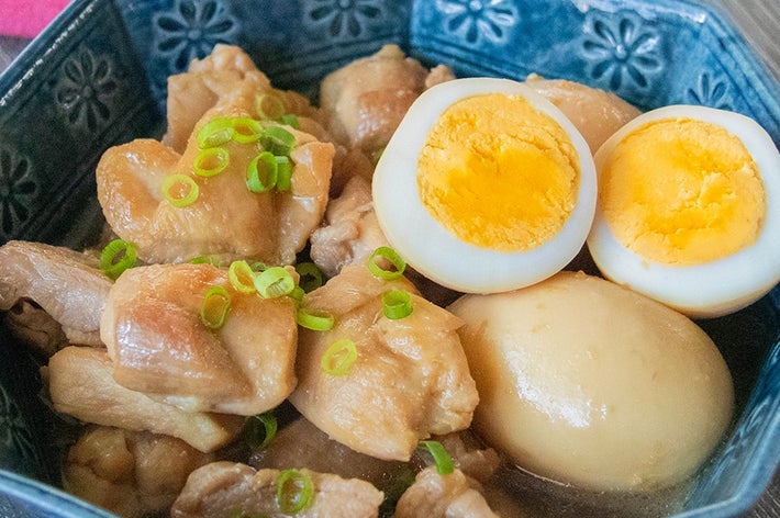 青い器に盛られた煮卵と鶏もも肉のしょうゆ煮。小ネギが散らされている。
