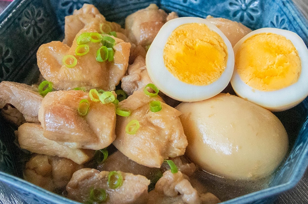 青い器に盛られた煮卵と鶏もも肉のしょうゆ煮。小ネギが散らされている。