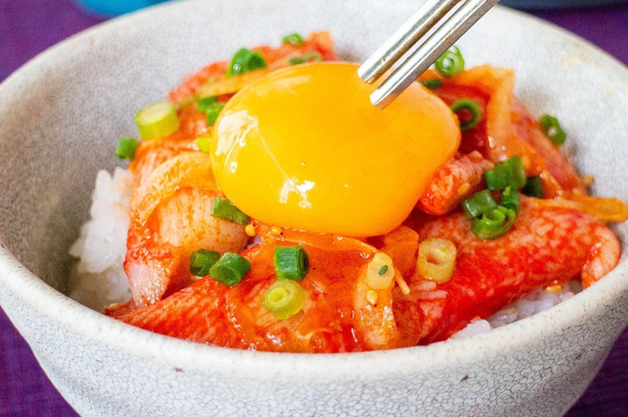 ご飯の上にキムチ、カニカマ、刻んだねぎが乗った丼。上に生卵黄が添えられている。
