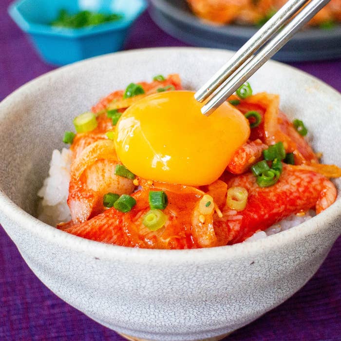 ご飯の上にキムチ、カニカマ、刻んだねぎが乗った丼。上に生卵黄が添えられている。