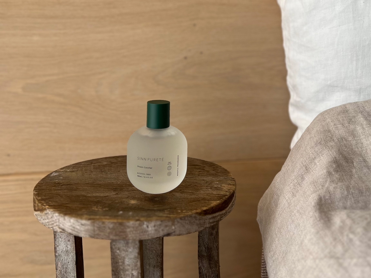 Perfume bottle on a wooden stool beside a bed with a wooden backdrop