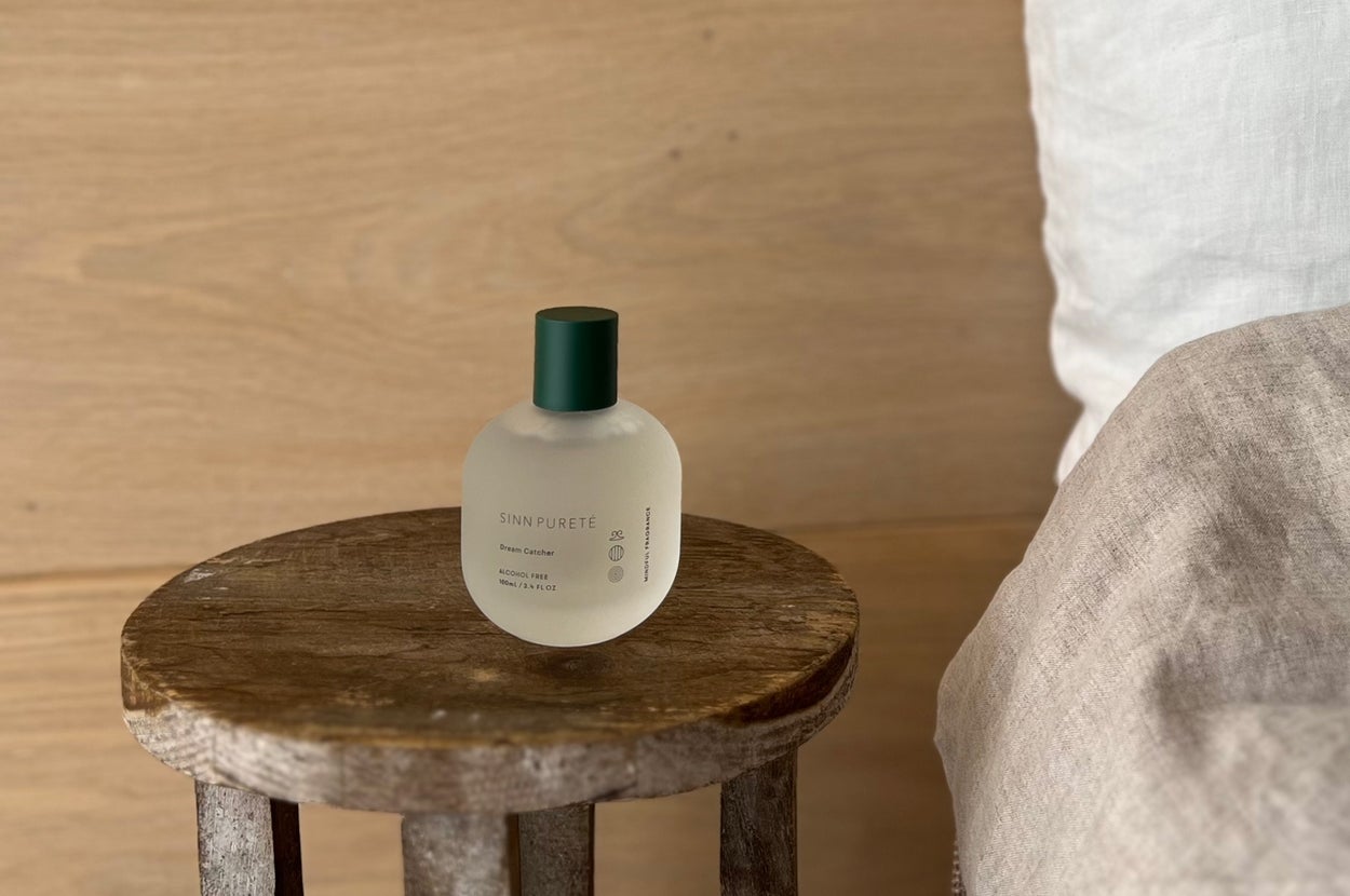 Perfume bottle on a wooden stool beside a bed with a wooden backdrop