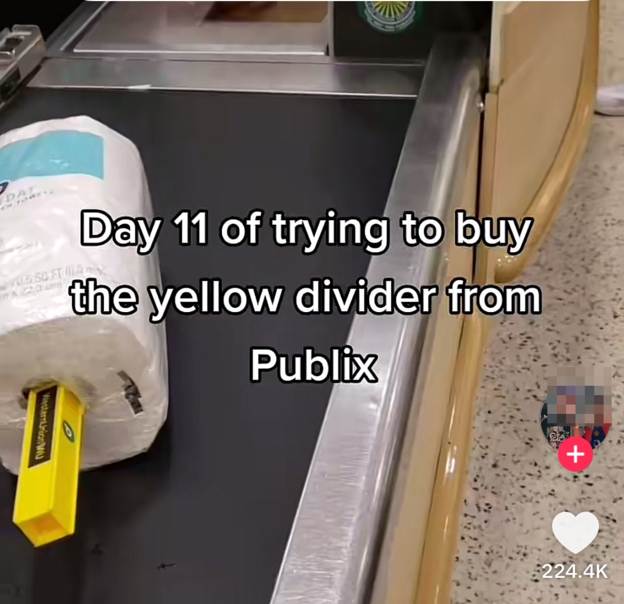 A supermarket checkout belt with a roll of paper towels and a yellow divider. Text reads: &quot;Day 11 of trying to buy the yellow divider from Publix.&quot;