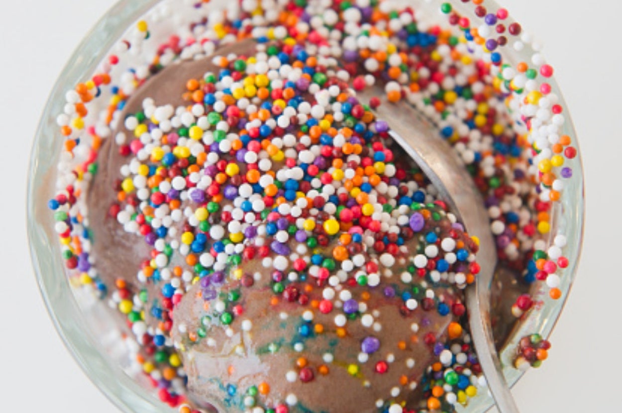 Chocolate ice cream sprinkled with colorful candy dots in a bowl, with a spoon on the side