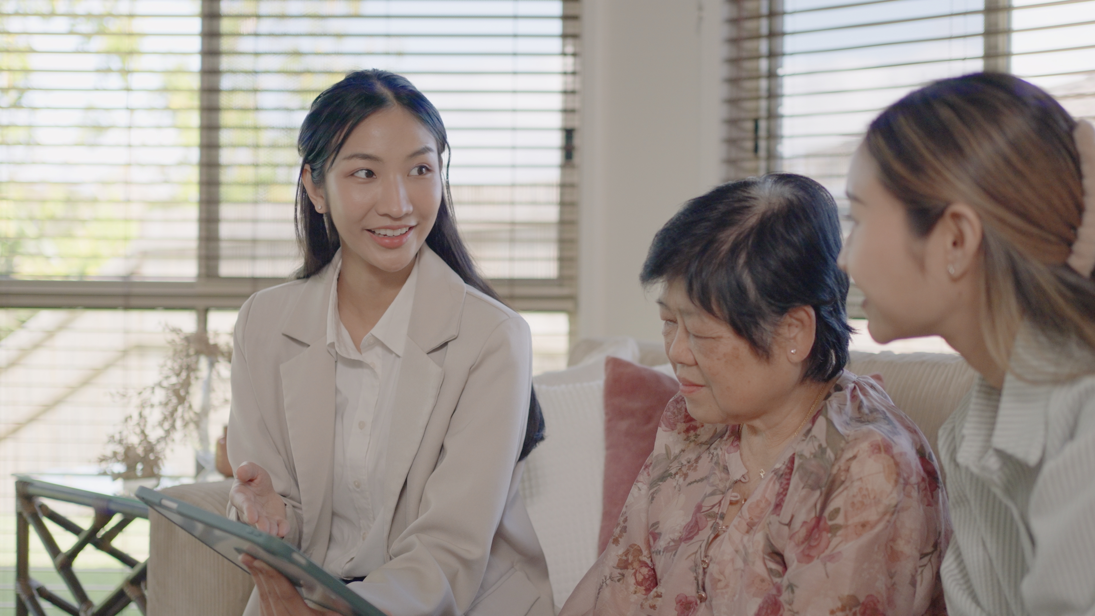 Tre kvinner sitter sammen på en sofa, engasjert i en vennlig samtale mens en viser noe på et nettbrett