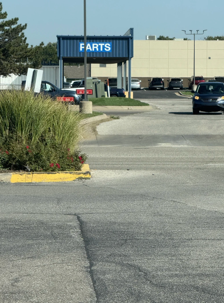 Auto parts store entrance with several cars in the parking lot visible in the background