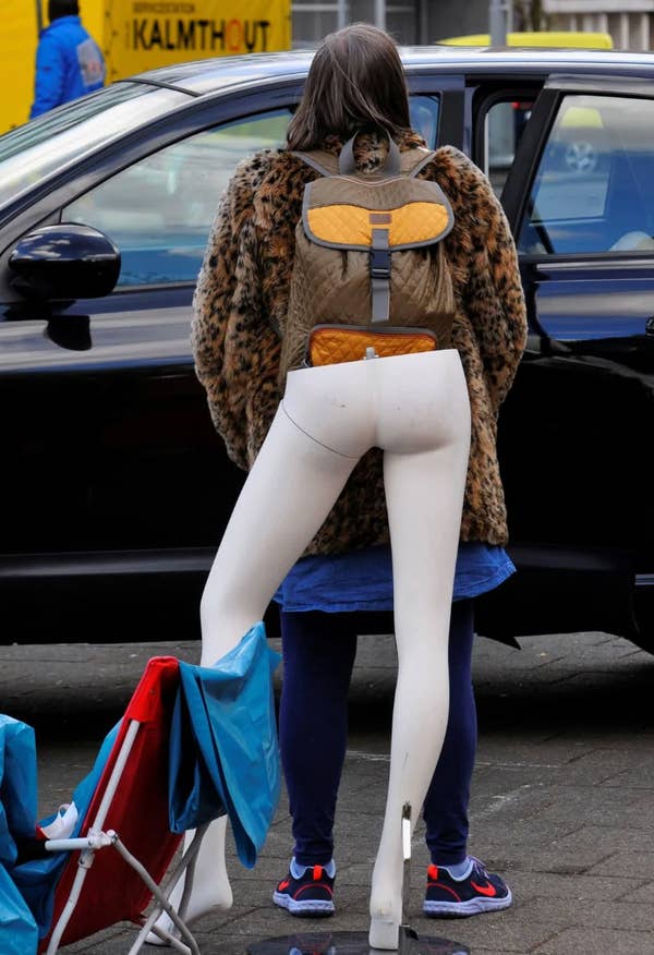 Person with a faux fur coat and backpack carries mannequin legs in a parking lot