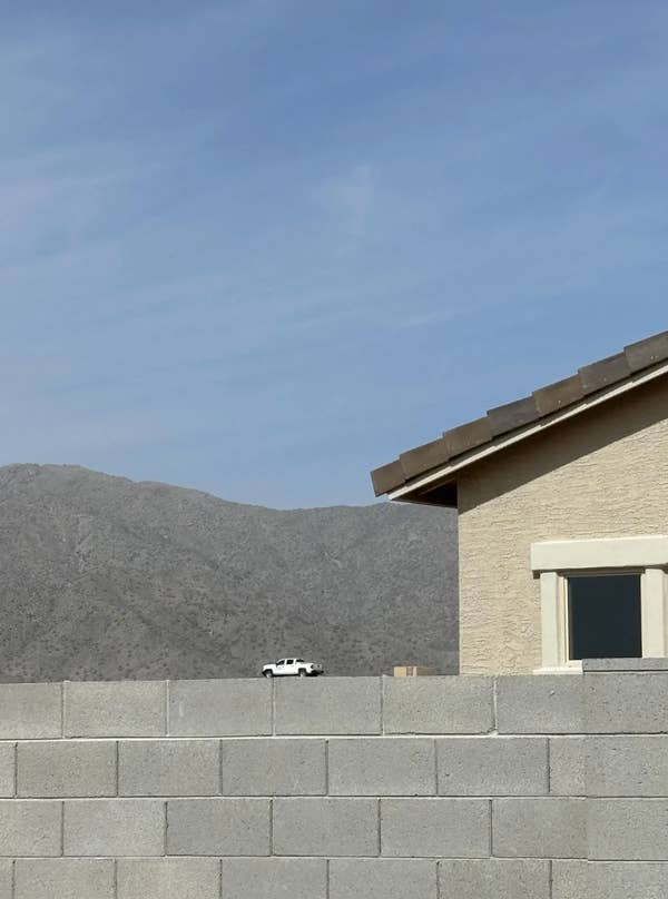 Toy car on brick wall appears like a real vehicle next to house, creating a humorous perspective illusion