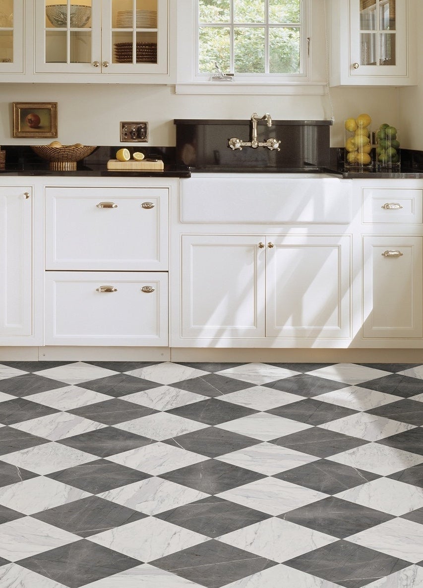 Kitchen with checkered floor, white cabinets, farmhouse sink, and a black countertop. Lemons and limes are placed by the window