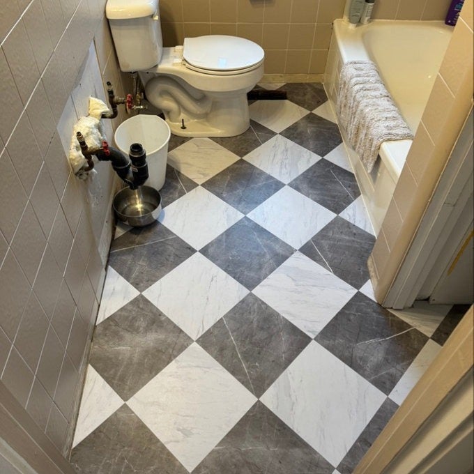 Bathroom with checkered tile floor, modern toilet, bathtub with a towel on the edge, and minimal decor for a sleek, functional style