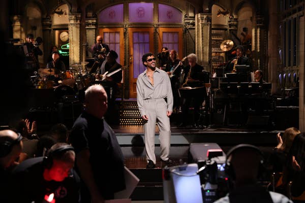 Bad Bunny on stage performing with a live band on a late-night TV set. Audience and crew present