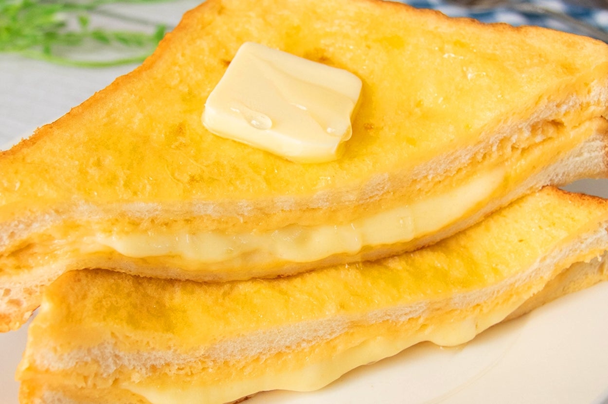チーズが挟まれたトーストにバターが乗った食欲をそそるサンドイッチが白い皿に置かれています。